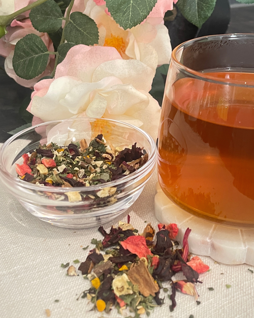 A glass of turmeric hibiscus  detox herbal tea  next to a small clear bowl filled with loose-leaf tea blend
